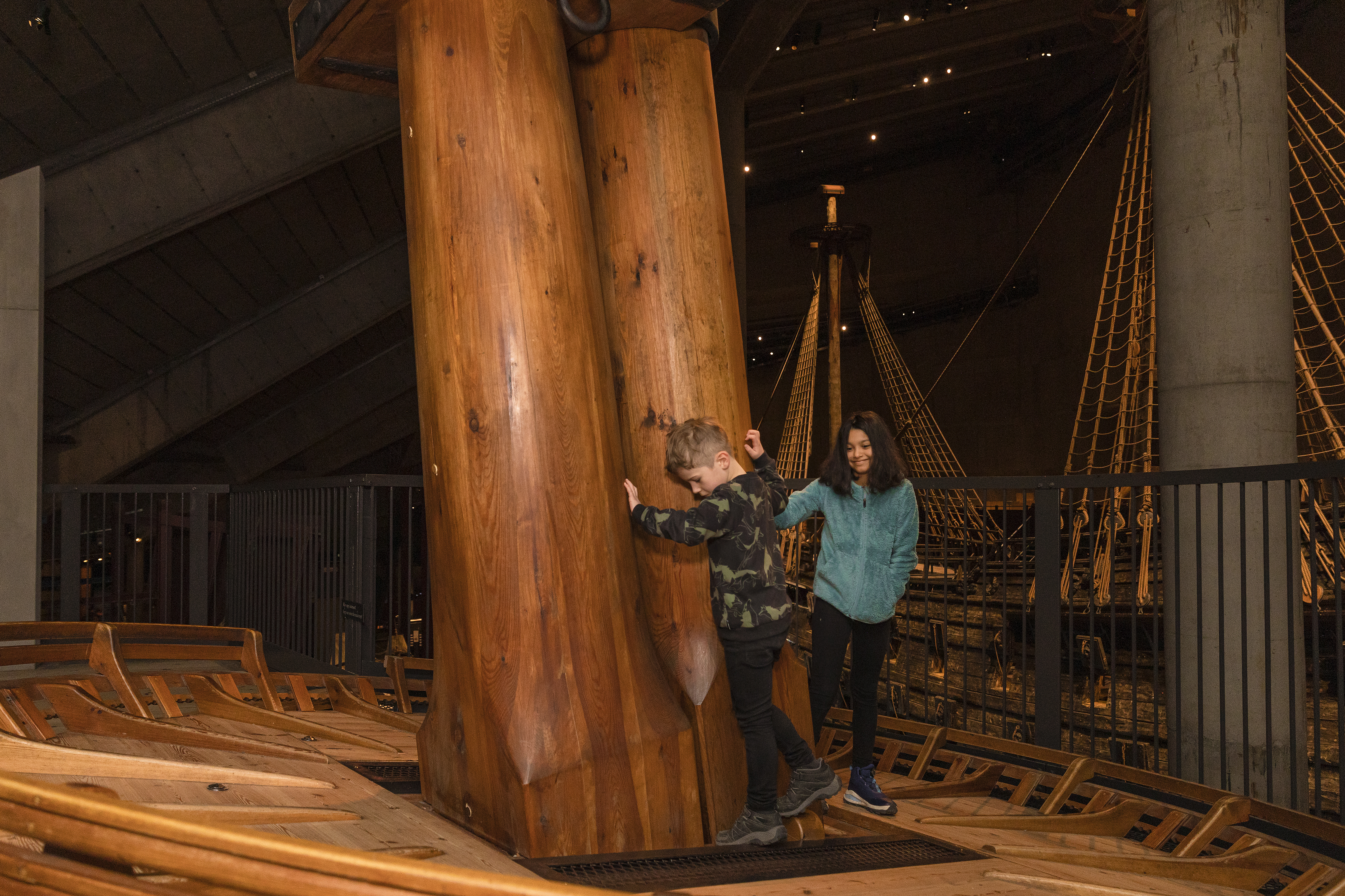 Två barn klättrar på Vasas modell av märs, högt upp i museet. Skeppet syns i bakgrunden. 