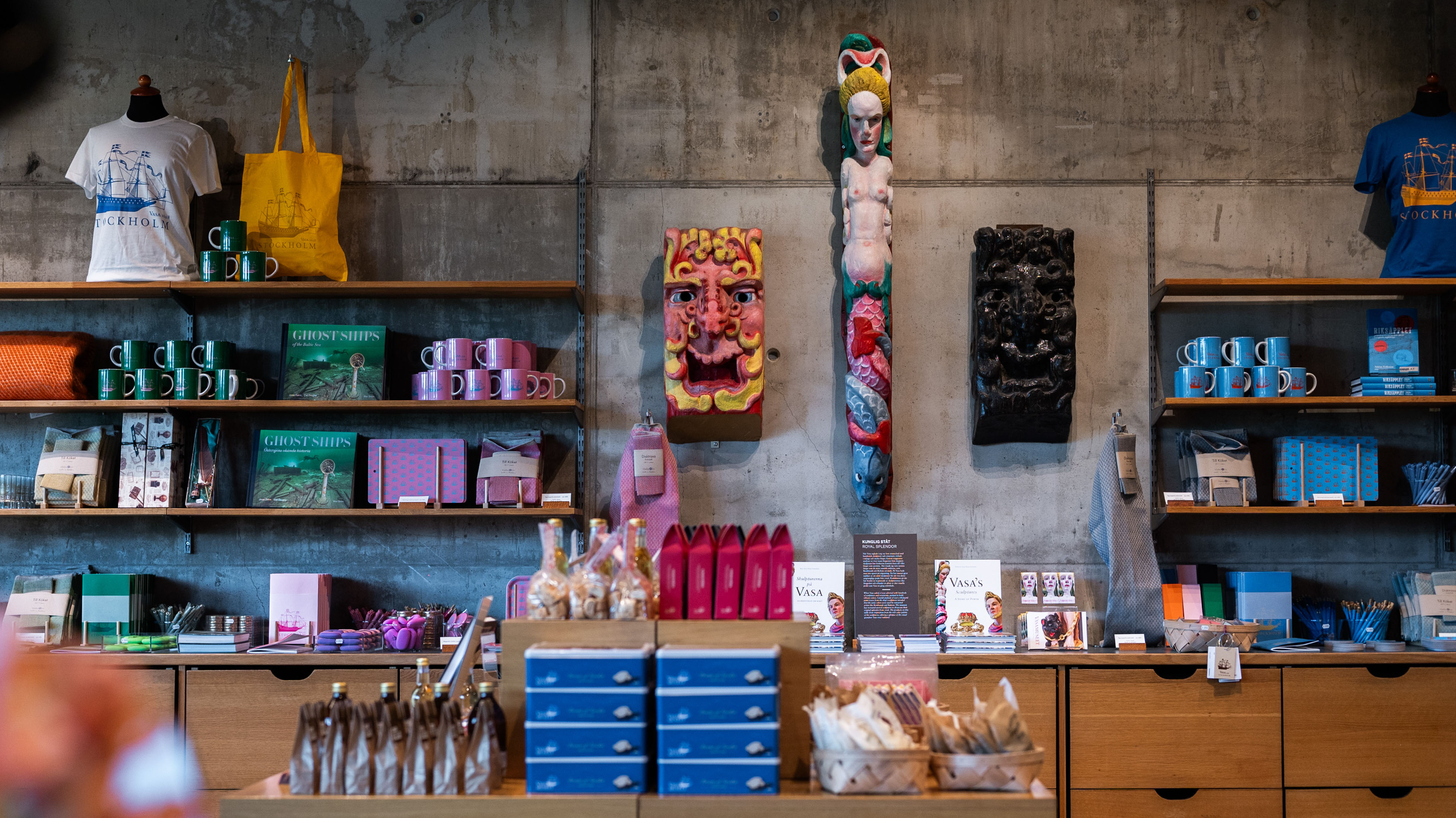 Butikshyllor i trä fyllda med varor däribland linnehanddukar, koppar och brickor med bilder av skeppet Vasa.
