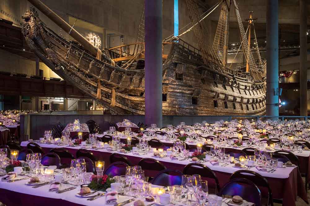 Bild på flera dukade bord som står framför Vasa. På borden står glas, tallrikar och LED-ljus.