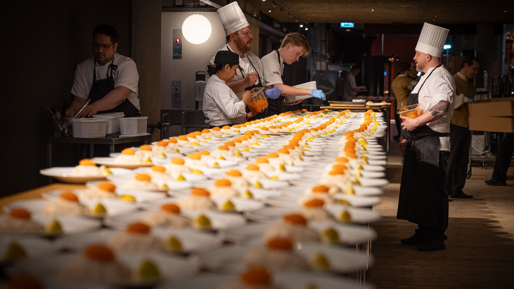 Kökspersonal i kockkläder arbetar vid långt bord med tallrikar med löjrom. 