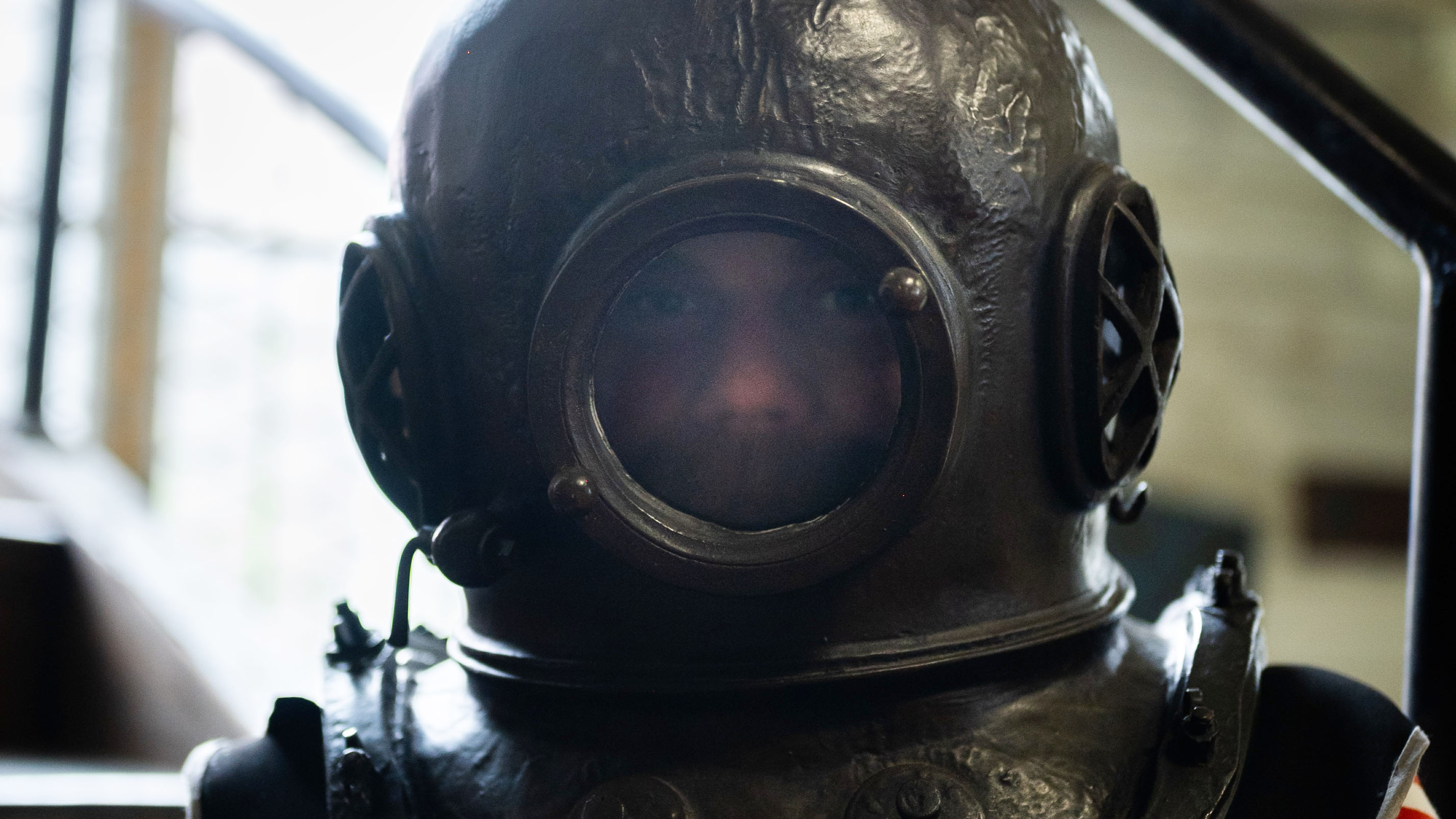 Gammaldags hjälm till tungdykardräkt, en person ser ut genom det runda glaset. 