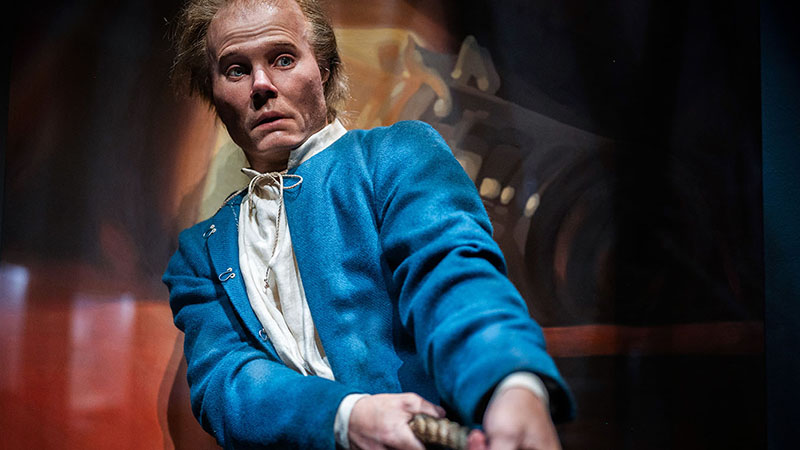 Foto av modell av man i blå Jacka och oroligt ansiktsuttryck i musei-utställning. 